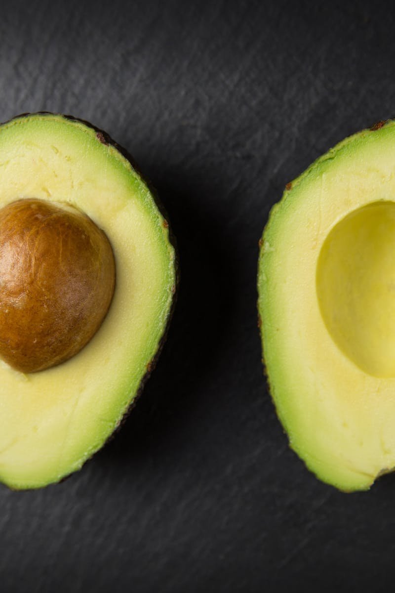 Close-up of fresh sliced avocado halves on a dark slate surface, showcasing healthy eating.